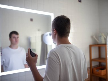 Erkek figürü parlak bir aynanın önünde, temiz bir banyo düzeneği ve sıcak bir atmosferle çevrili bir aletle tımar etme faaliyetlerine girişiyor.