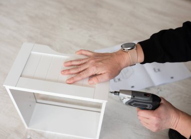 Kablosuz tornavidayı kullanarak yere, mobilya mağazasına ya da ev servisine beyaz ahşap dolap monte eden kişi.