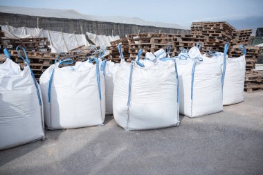 Asfalt, küresel lojistik, depo, nakliye sahasında büyük beyaz sanayi çantaları sıralanmış..