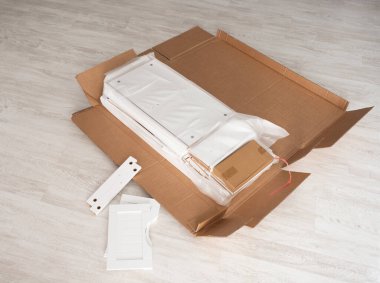 Evdeki yeni mobilya montaj süreci, beyaz kabine parçaları modern ışıklı döşeme döşemesinde ambalaj kartonunda yatıyor..