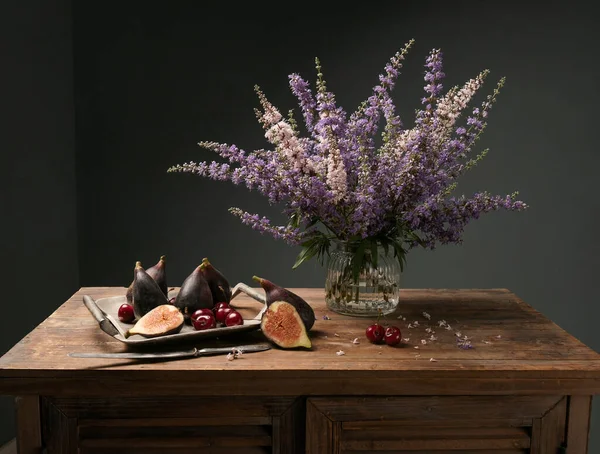 Olgun incirlerle ve vazoda kır çiçekleriyle nefis bir kompozisyon klasik resim tarzı karanlık bir tabloda eski ahşap masa üzerinde..