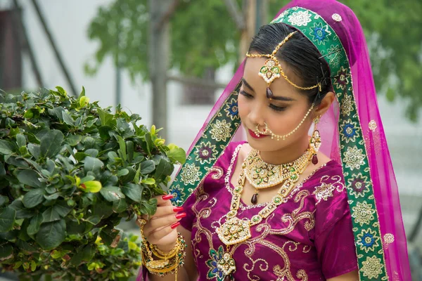 미디엄은 인도의 자홍색 사리를 식물에 솔질하면서 아시아 여성의 초상화를 — 스톡 사진
