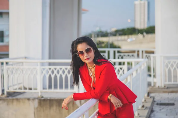 Close up Asian woman in a red jacket posting next to a white fence, She put her elbows on the white fence on the bridge with urban background