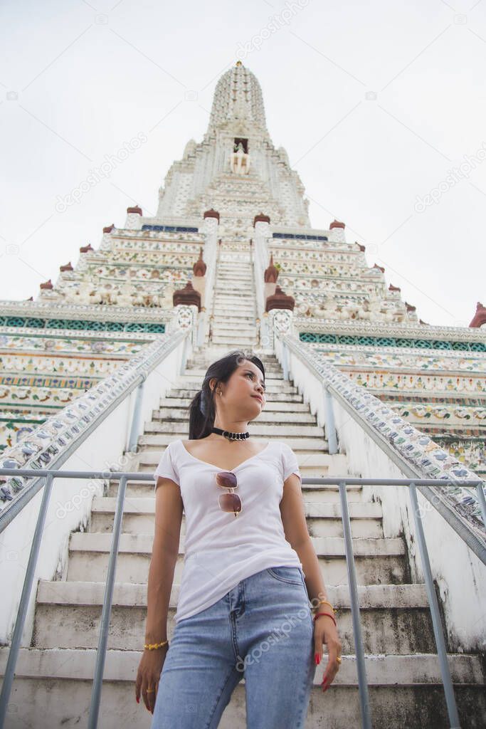 Lowangle view Portrait beautiful Asian woman in a white T-shirt looking away at the Wat Arun temple while traveling in Thailand.