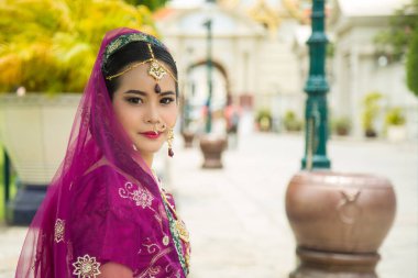 Mor Hint geleneksel sarisi giyen çekici Asyalı kadın yeşil doğa duvarlı bir kameraya bakıyor..