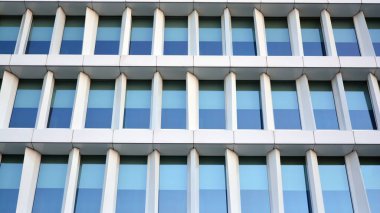 Mavi gökyüzünün altındaki tonlu cam ve çelik yapılardan yapılmış mavi perde duvarı. Bir binanın parçası..