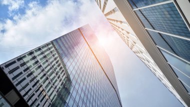 İş bölgesindeki modern ofis binalarının alt manzarası. Gökdelen cam cepheleri masmavi gökyüzünde güneş ışınlarıyla aydınlık bir günde.