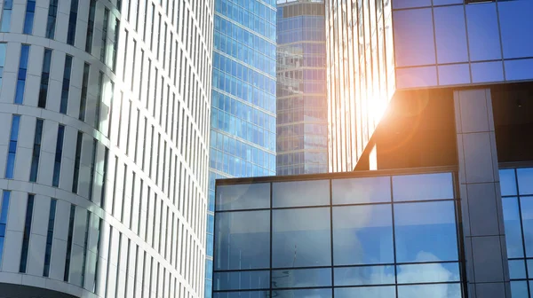 Blue curtain wall made of toned glass and steel constructions under blue sky. A fragment of a building. Glass facades on a bright sunny day with sunbeams in the blue sky.