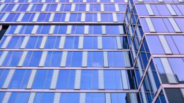 Mavi gökyüzünün altındaki tonlu cam ve çelik yapılardan yapılmış mavi perde duvarı. Bir binanın parçası..