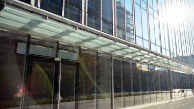 Mavi gökyüzünün altındaki tonlu cam ve çelik yapılardan yapılmış mavi perde duvarı. Binanın bir parçası. Parlak güneşli bir günde mavi gökyüzünde güneş ışınlarıyla cam cepheler..