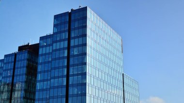 Mavi gökyüzünün altındaki tonlu cam ve çelik yapılardan yapılmış mavi perde duvarı. Bir binanın parçası..