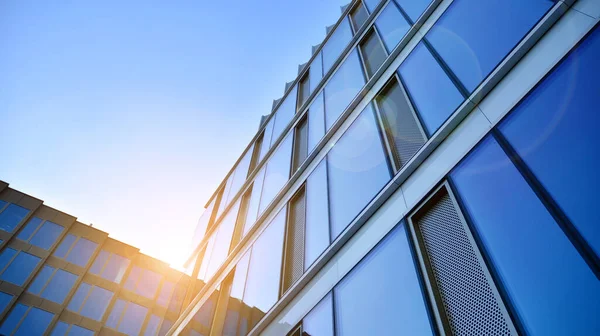 Blue curtain wall made of toned glass and steel constructions under blue sky. A fragment of a building. Glass facades on a bright sunny day with sunbeams in the blue sky.