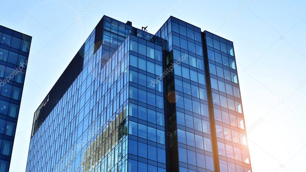 Blue curtain wall made of toned glass and steel constructions under blue sky. A fragment of a building. Glass facades on a bright sunny day with sunbeams in the blue sky.