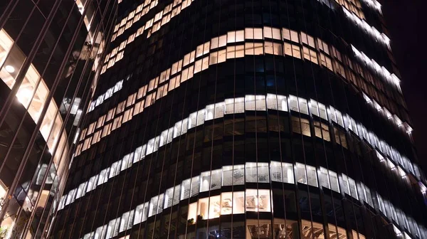 Pattern of office buildings windows illuminated at night. Lighting with Glass architecture facade design with reflection in urban city.