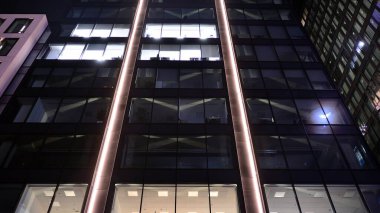 Ofis binalarının pencereleri gece aydınlandı. Şehir merkezinde yansıması olan cam mimari cephe tasarımı ile ışıklandırma.