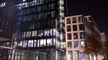 Ofis binalarının pencereleri gece aydınlandı. Şehir merkezinde yansıması olan cam mimari cephe tasarımı ile ışıklandırma.