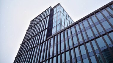 Aşağıdan yukarıya kar yağarken modern bir ofis binasının cephesi