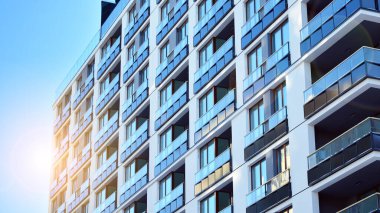 Mavi gökyüzü olan güneşli bir günde modern apartman binaları. Modern bir apartmanın ön cephesi. Güneş ışığıyla kaplı cam yüzey..