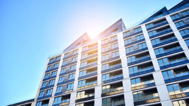 Mavi gökyüzü olan güneşli bir günde modern apartman binaları. Modern bir apartmanın ön cephesi. Güneş ışığıyla kaplı cam yüzey..