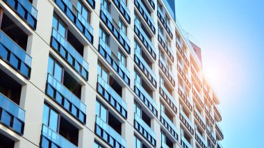 Mavi gökyüzü olan güneşli bir günde modern apartman binaları. Modern bir apartmanın ön cephesi. Güneş ışığıyla kaplı cam yüzey..