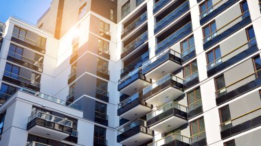 Mavi gökyüzü olan güneşli bir günde modern apartman binaları. Modern bir apartmanın ön cephesi. Güneş ışığıyla kaplı cam yüzey..