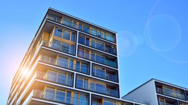 Mavi gökyüzü olan güneşli bir günde modern apartman binaları. Modern bir apartmanın ön cephesi. Güneş ışığıyla kaplı cam yüzey..