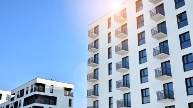 Mavi gökyüzü olan güneşli bir günde modern apartman binaları. Modern bir apartmanın ön cephesi. Güneş ışığıyla kaplı cam yüzey..