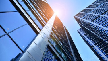 Mavi gökyüzüne karşı modern gökdelenlerin alt manzarası. Şehir merkezindeki iş binalarına bakıyorum. Ufukta yükselen güneş.