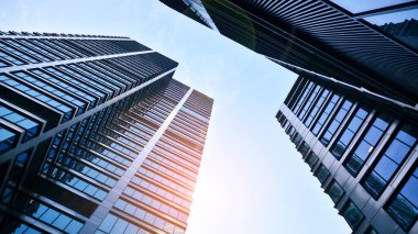 Mavi gökyüzüne karşı modern gökdelenlerin alt manzarası. Şehir merkezindeki iş binalarına bakıyorum. Ufukta yükselen güneş.