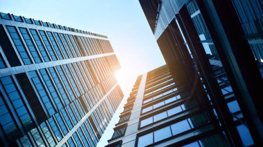 Mavi gökyüzüne karşı modern gökdelenlerin alt manzarası. Şehir merkezindeki iş binalarına bakıyorum. Ufukta yükselen güneş.