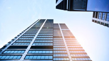 Mavi gökyüzüne karşı modern gökdelenlerin alt manzarası. Şehir merkezindeki iş binalarına bakıyorum. Ufukta yükselen güneş.