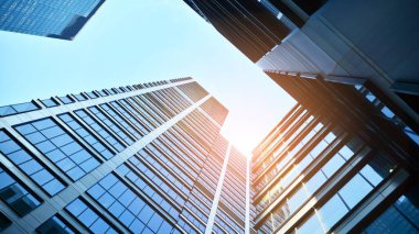 Mavi gökyüzüne karşı modern gökdelenlerin alt manzarası. Şehir merkezindeki iş binalarına bakıyorum. Ufukta yükselen güneş.