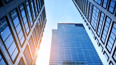 Mavi gökyüzüne karşı modern gökdelenlerin alt manzarası. Şehir merkezindeki iş binalarına bakıyorum. Ufukta yükselen güneş.