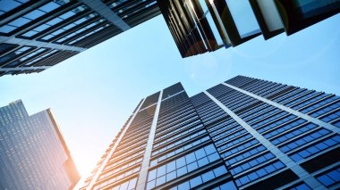 Mavi gökyüzüne karşı modern gökdelenlerin alt manzarası. Şehir merkezindeki iş binalarına bakıyorum. Ufukta yükselen güneş.