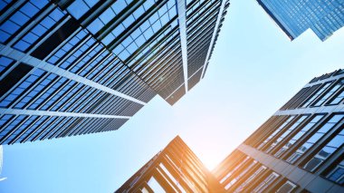 Mavi gökyüzüne karşı modern gökdelenlerin alt manzarası. Şehir merkezindeki iş binalarına bakıyorum. Ufukta yükselen güneş.
