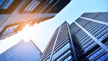 Mavi gökyüzüne karşı modern gökdelenlerin alt manzarası. Şehir merkezindeki iş binalarına bakıyorum. Ufukta yükselen güneş.