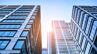 Mavi gökyüzüne karşı modern gökdelenlerin alt manzarası. Şehir merkezindeki iş binalarına bakıyorum. Ufukta yükselen güneş.