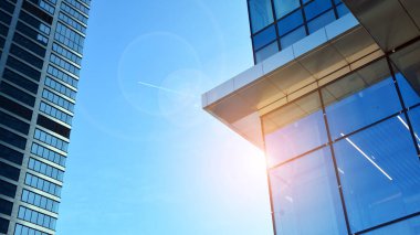 Şehir merkezindeki işletme bölgesi mimarisi. Mavi gökyüzüne ve güneş ışığına karşı cam yansıtıcı ofis binaları. Ekonomi, finans, iş faaliyeti konsepti. Ufukta yükselen güneş.