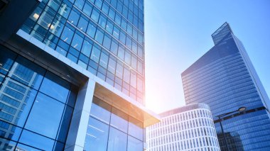 Şehir merkezindeki işletme bölgesi mimarisi. Mavi gökyüzüne ve güneş ışığına karşı cam yansıtıcı ofis binaları. Ekonomi, finans, iş faaliyeti konsepti. Ufukta yükselen güneş.