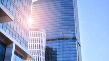 Şehir merkezindeki işletme bölgesi mimarisi. Mavi gökyüzüne ve güneş ışığına karşı cam yansıtıcı ofis binaları. Ekonomi, finans, iş faaliyeti konsepti. Ufukta yükselen güneş.