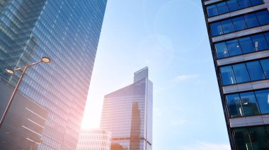 Şehir merkezindeki işletme bölgesi mimarisi. Mavi gökyüzüne ve güneş ışığına karşı cam yansıtıcı ofis binaları. Ekonomi, finans, iş faaliyeti konsepti. Ufukta yükselen güneş.
