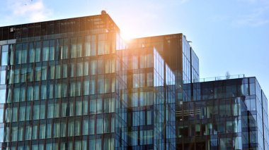 Binanın cam cephesinde mavi gökyüzü yansıması. Gün doğumu, yansıma ve perspektif ile kapalı ofis binası pencereleri mavi gökyüzünde güneş ışınları ile aydınlık bir günde cam cephe. 