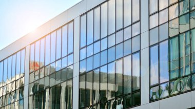 Binanın cam cephesinde mavi gökyüzü yansıması. Gün doğumu, yansıma ve perspektif ile kapalı ofis binası pencereleri mavi gökyüzünde güneş ışınları ile aydınlık bir günde cam cephe. 