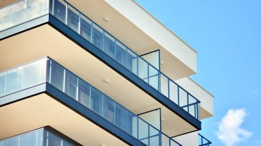 Modern mimarinin bir parçası, duvarlar ve cam. Mavi gökyüzüne karşı bir apartmanın pencere ve balkonları. New Lüks Ev ve Ev Kompleksinin ayrıntıları. Şehir gayrimenkul ve konut mimarisinin bir parçası..  