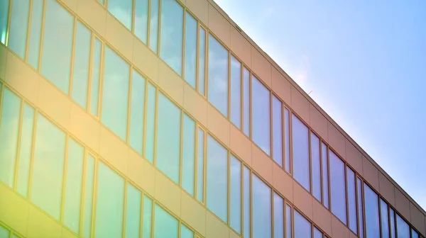 Blue sky reflection in glass facade of building. View of office building windows close up with sunrise, reflection and perspective.. Glass facade on a bright sunny day with sunbeams on the blue sky.