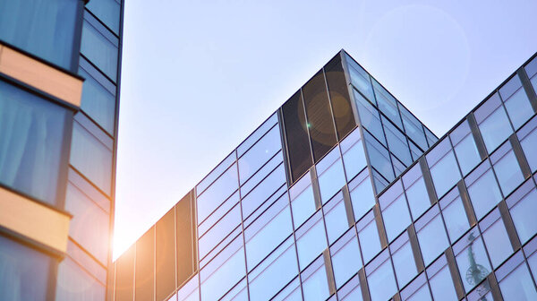 Blue sky reflection in glass facade of building. View of office building windows close up with sunrise, reflection and perspective.. Glass facade on a bright sunny day with sunbeams on the blue sky.