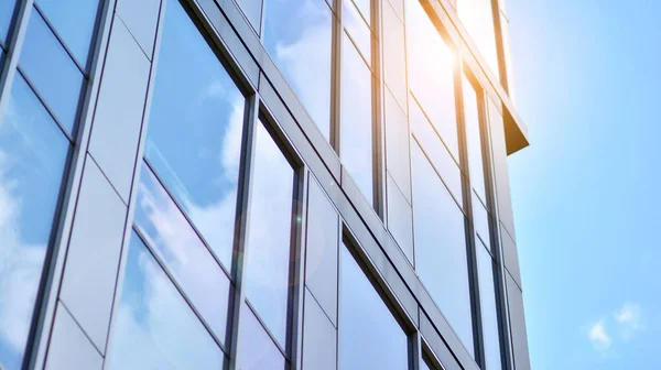 Blue sky reflection in glass facade of building. View of office building windows close up with sunrise, reflection and perspective.. Glass facade on a bright sunny day with sunbeams on the blue sky.