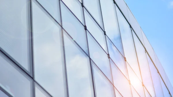 Blue sky reflection in glass facade of building. View of office building windows close up with sunrise, reflection and perspective.. Glass facade on a bright sunny day with sunbeams on the blue sky.