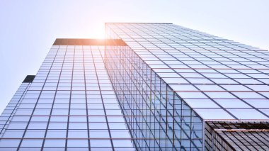 Güneş ışınlı modern mimari. Parlak güneşli bir günde mavi gökyüzünde güneş ışınları olan cam ve çelik cephe. Ekonomi, finans, iş faaliyeti kavramı.