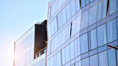 Modern cam bina ve yükselen güneş. Parlak güneşli bir günde mavi gökyüzünde güneş ışınlarıyla cam cephe. Ekonomi, finans, iş faaliyeti kavramı.  